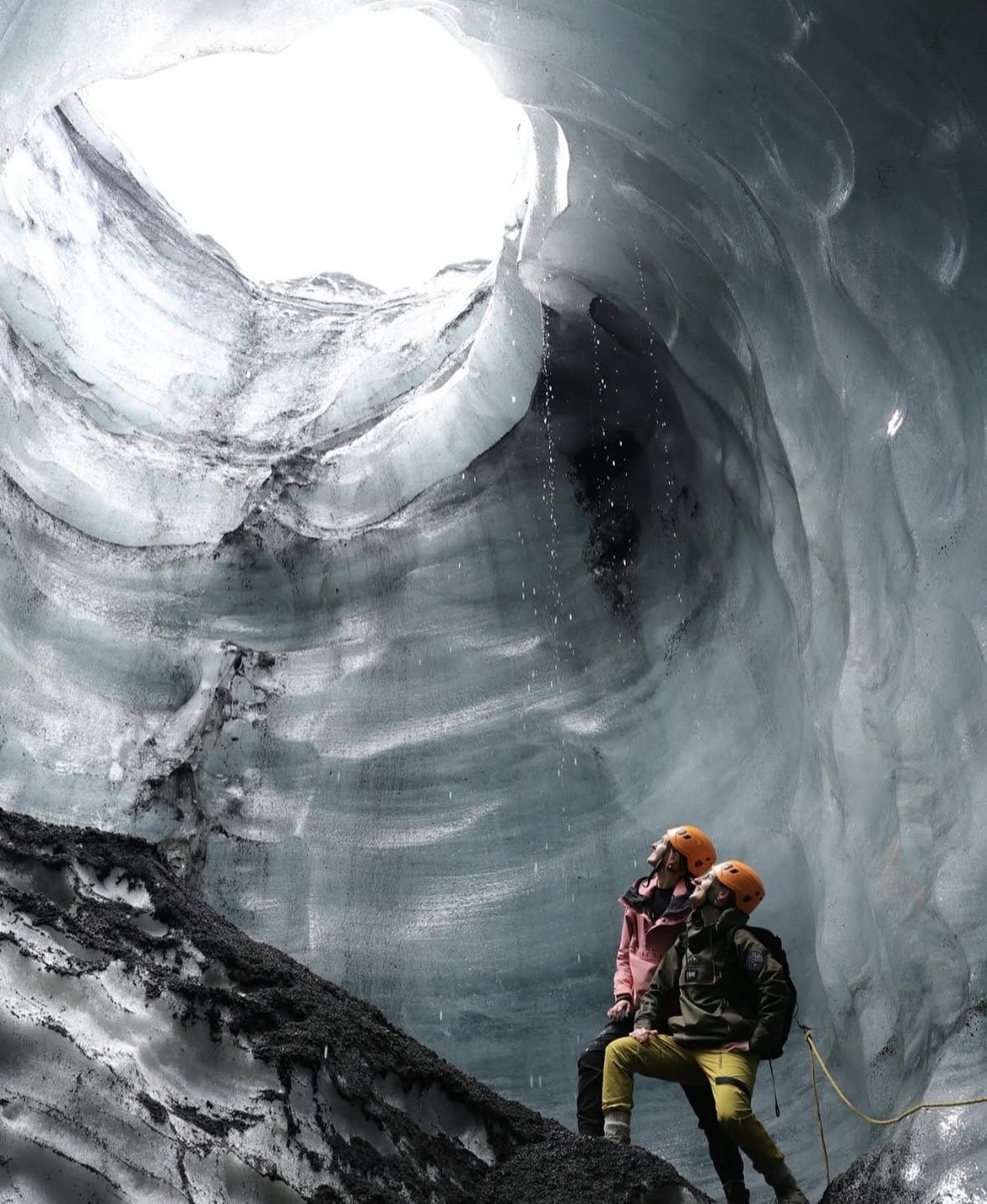 Tour guide leading a small group through the black and blue ice formations inside the Katla Ice Cave in Iceland